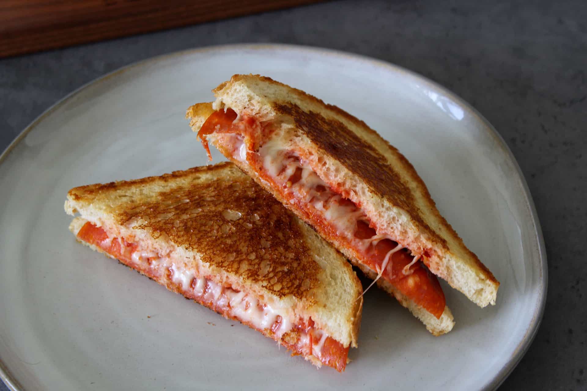 A cheesy pepperoni pizza panini sliced in half and stacked on a plate