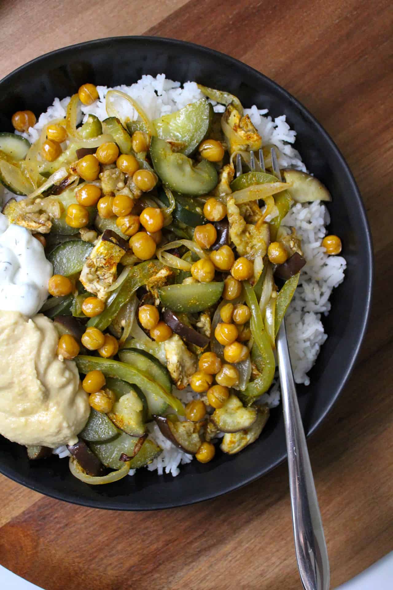 A rice bowl with Mediterranean roasted veggies, chickpeas, hummus, and tzatziki