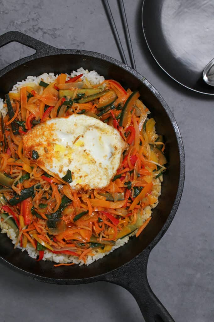 A cast iron skillet with vegetarian bibimbap, topped with a fried egg
