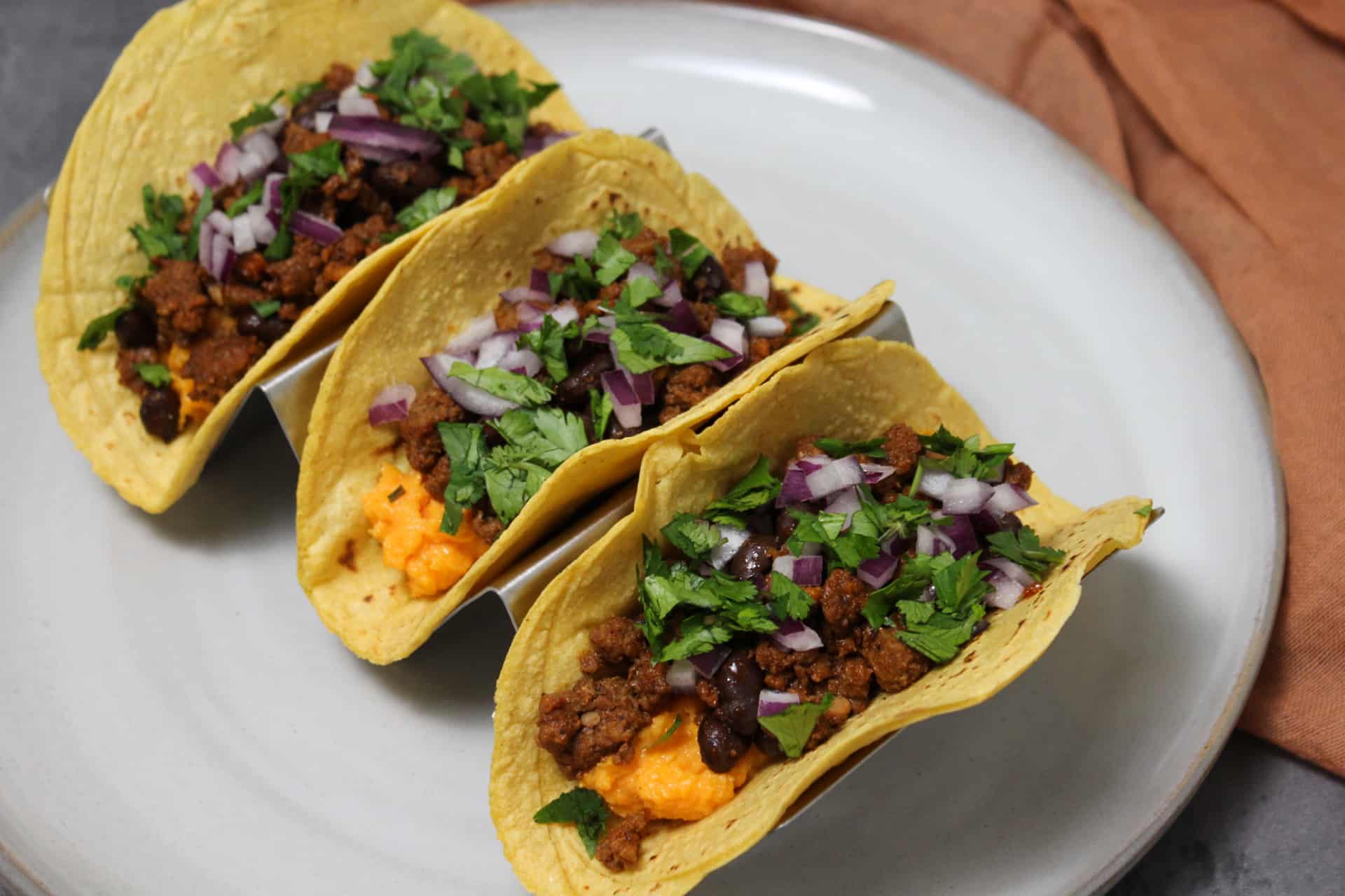 Three tacos made with mashed sweet potato, chorizo, and black beans in corn tortillas