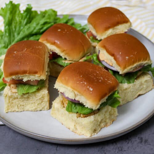 A plate of grilled chicken sliders on brioche buns with lettuce, tomato, and onion
