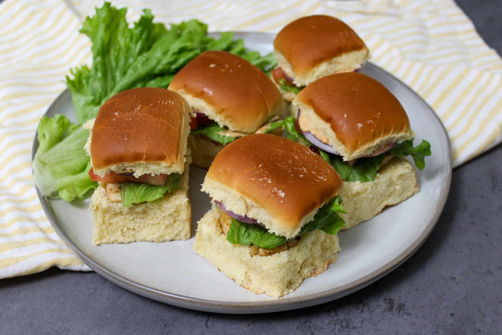 A plate of grilled chicken sliders on brioche buns with lettuce, tomato, and onion
