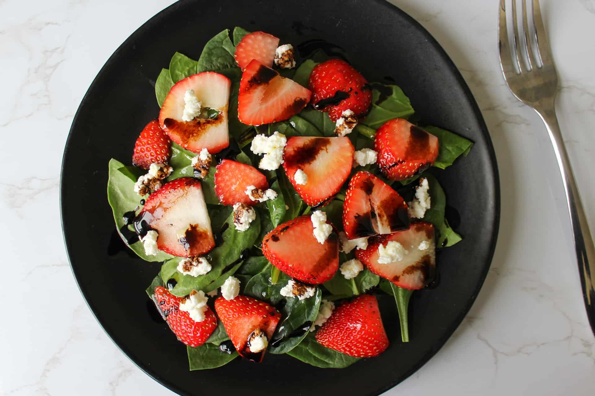 A strawberry spinach goat cheese salad with balsamic and olive oil on a plate