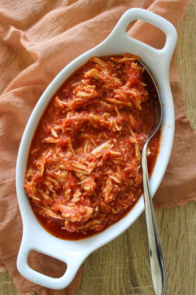 A dish of shredded slow cooker chicken parmesan in tomato sauce