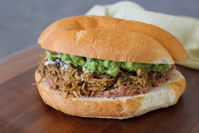 A carnitas torta made with pork, guacamole, refried beans, and queso fresco