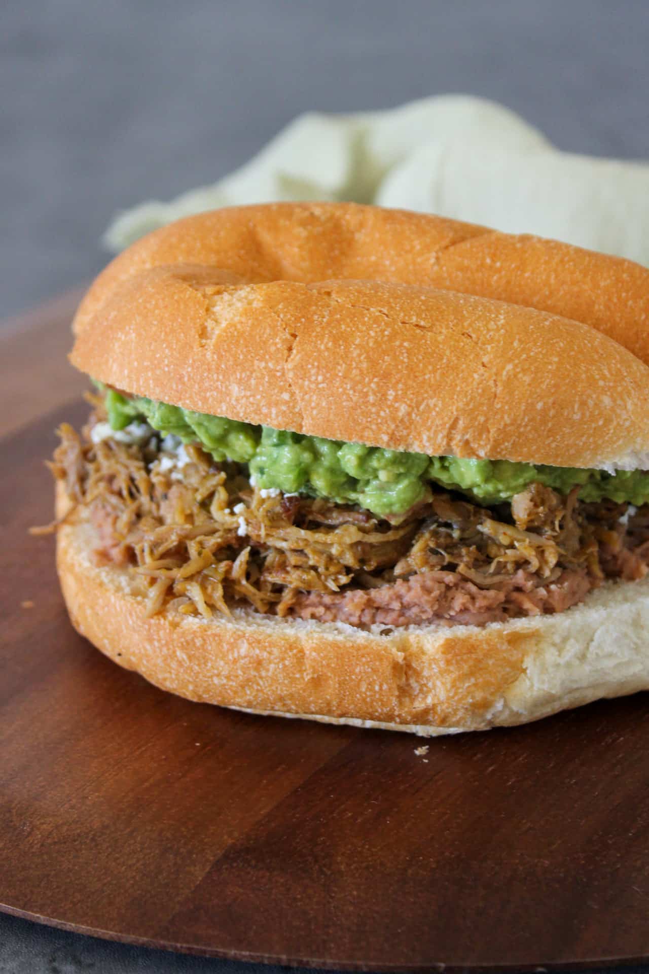 A Mexican carnitas pork torta with guacamole, refried beans, queso fresco, and salsa verde