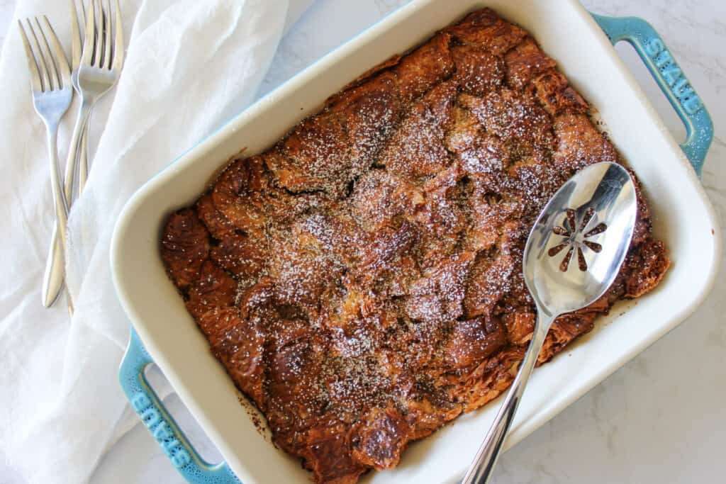 A croissant french toast bake with a serving spoon in a casserole dish