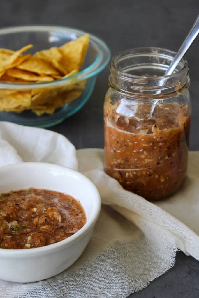 A jar of homemade fire roasted salsa with tortilla chips for serving