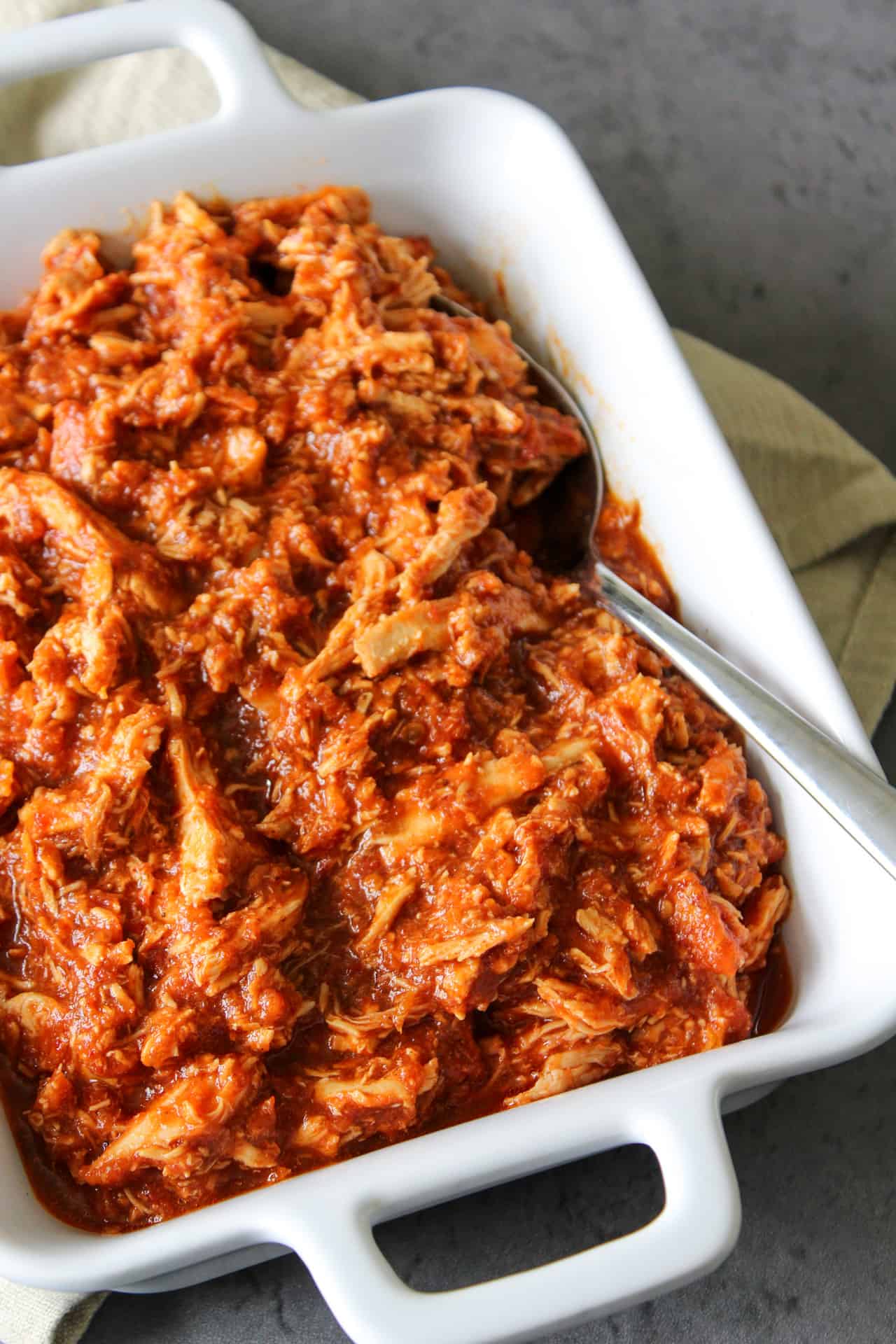Shredded chipotle chicken made in a slow cooker and served in a white serving dish.