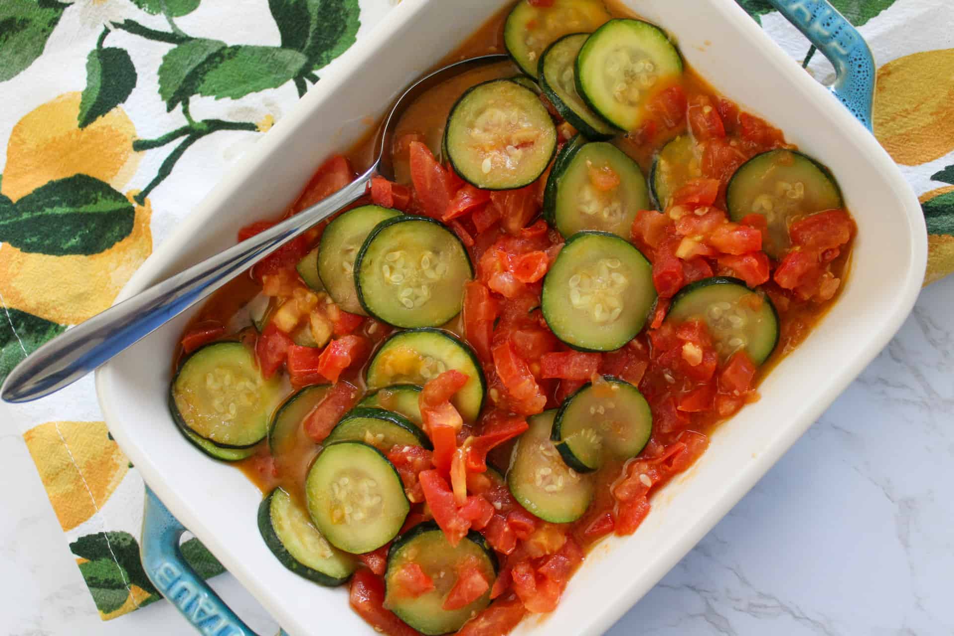 Summer squash and tomato side dish in a serving dish with a spoon