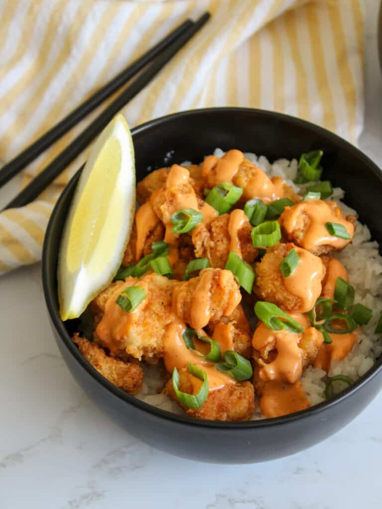 An Asian inspired fried fish rice bowl served with a lemon wedge