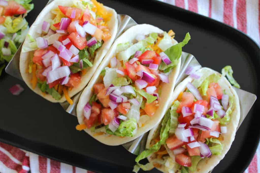 Three cheeseburger tacos with lettuce, tomato, and onion for toppings