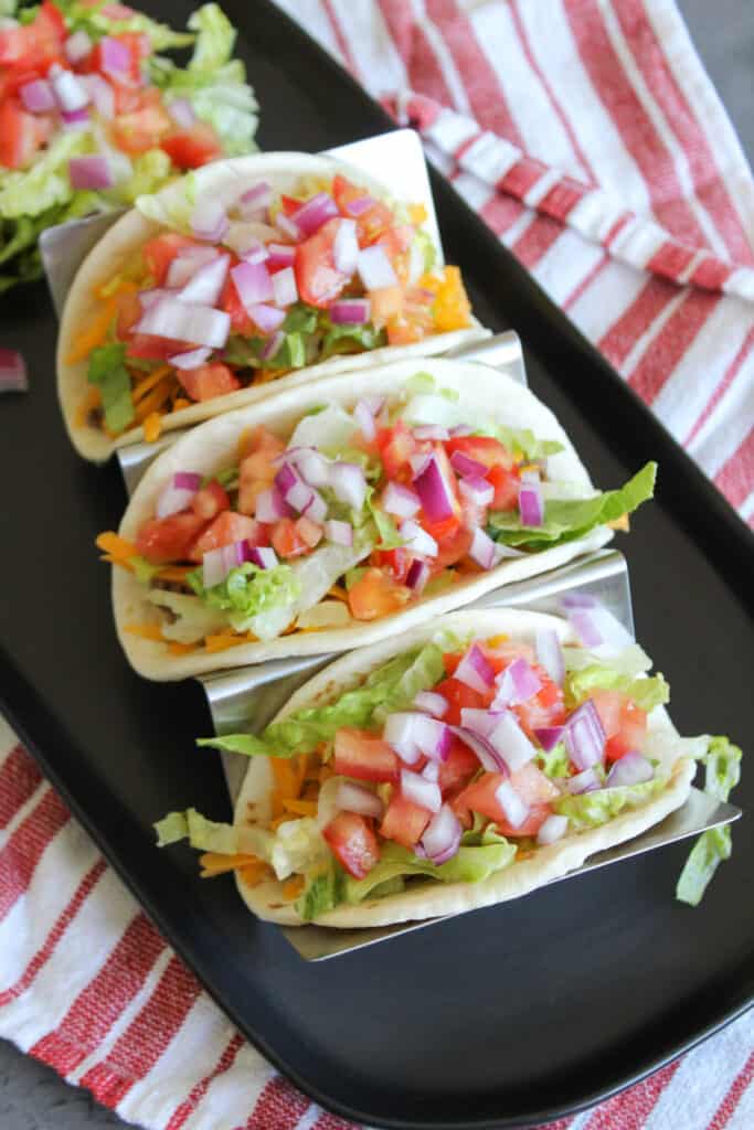 Three cheeseburger tacos with lettuce, tomato, and onion toppings