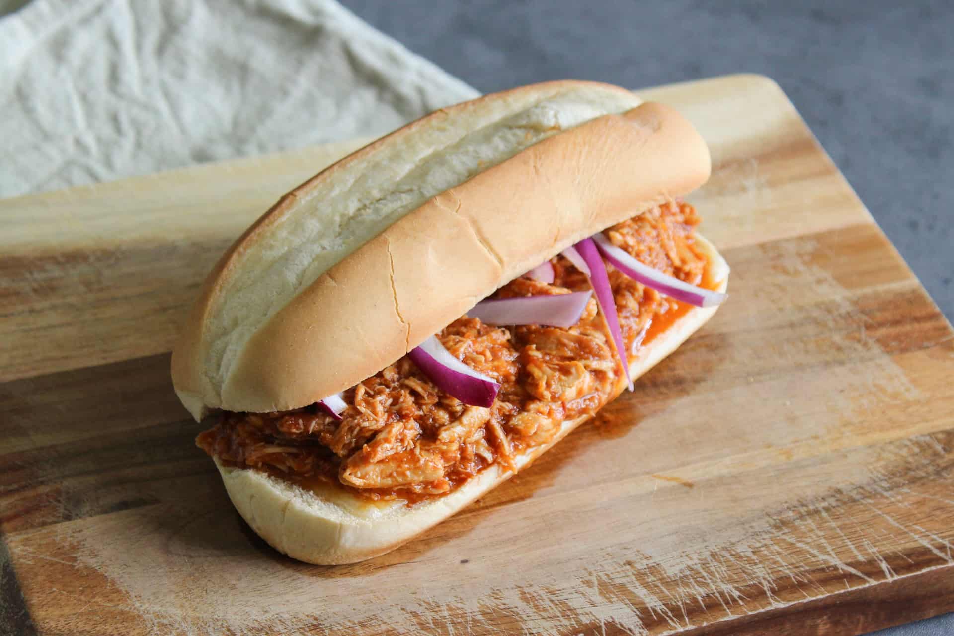 Shredded chipotle chicken on a sandwich roll with cheese and red onion