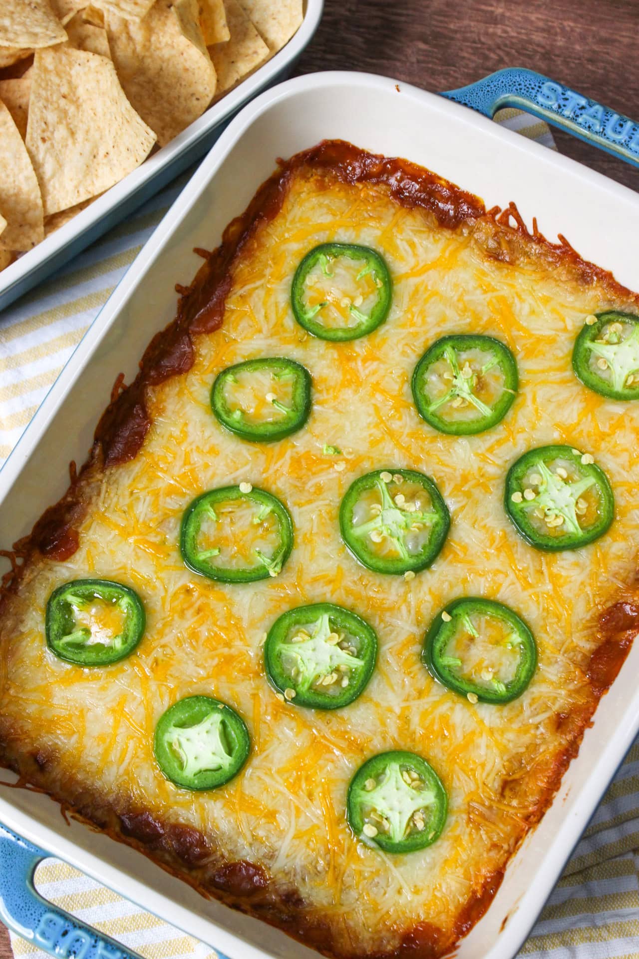 4 layer Mexican dip with the top being cheese and jalapeno wheels in a white and blue serving dish.