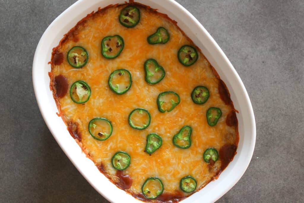 A hot layered Mexican dip with cheese and jalapenos in a serving dish.
