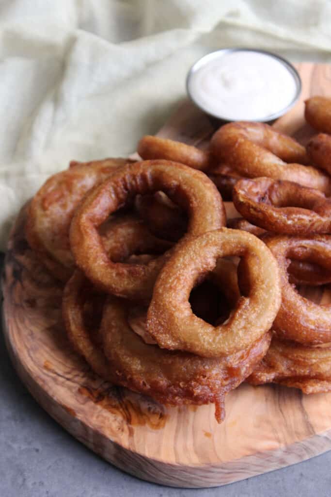 Beer battered onion rings on a serving board with ranch for dipping.