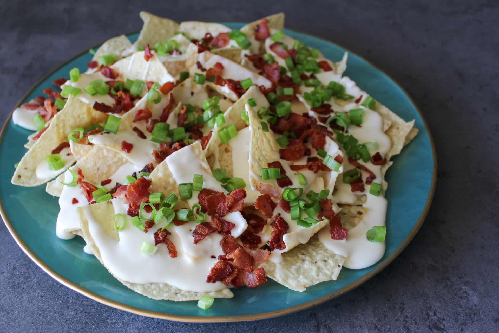 A plate of beer cheese pub nachos with bacon and scallions.