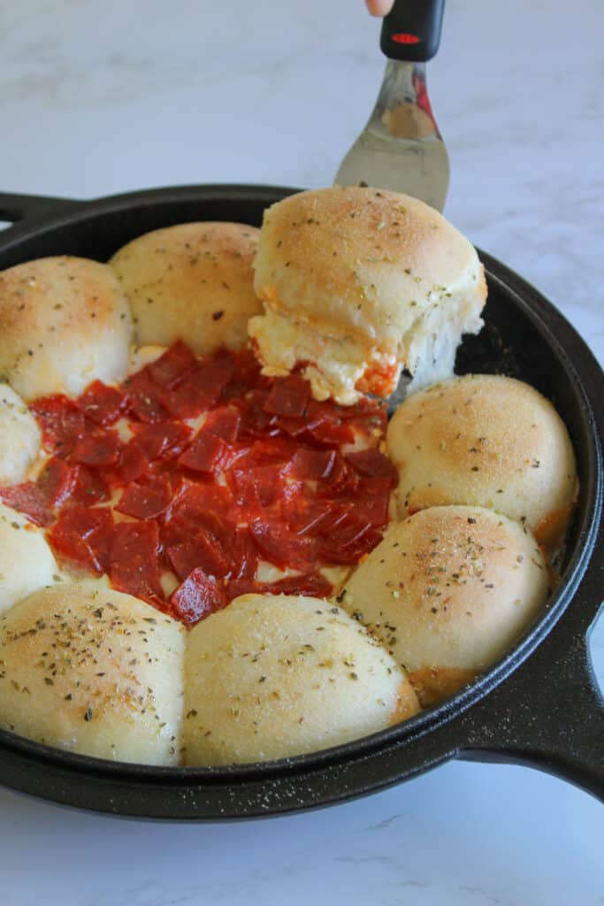 A spatula taking a dinner roll out of a skillet with pizza dip.