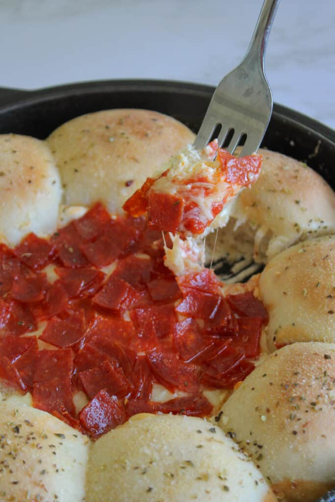 A fork digging into skillet pepperoni pizza dip.