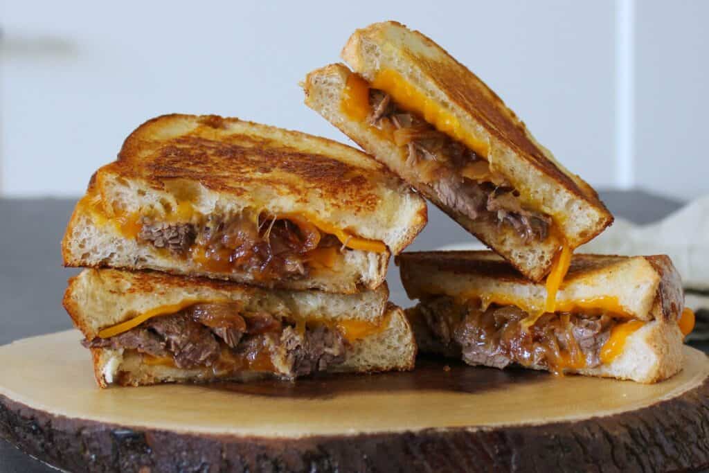 Two braised short rib grilled cheese sandwiches cut in half on a plate.