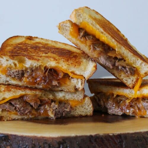 Two braised short rib grilled cheese sandwiches cut in half on a plate.