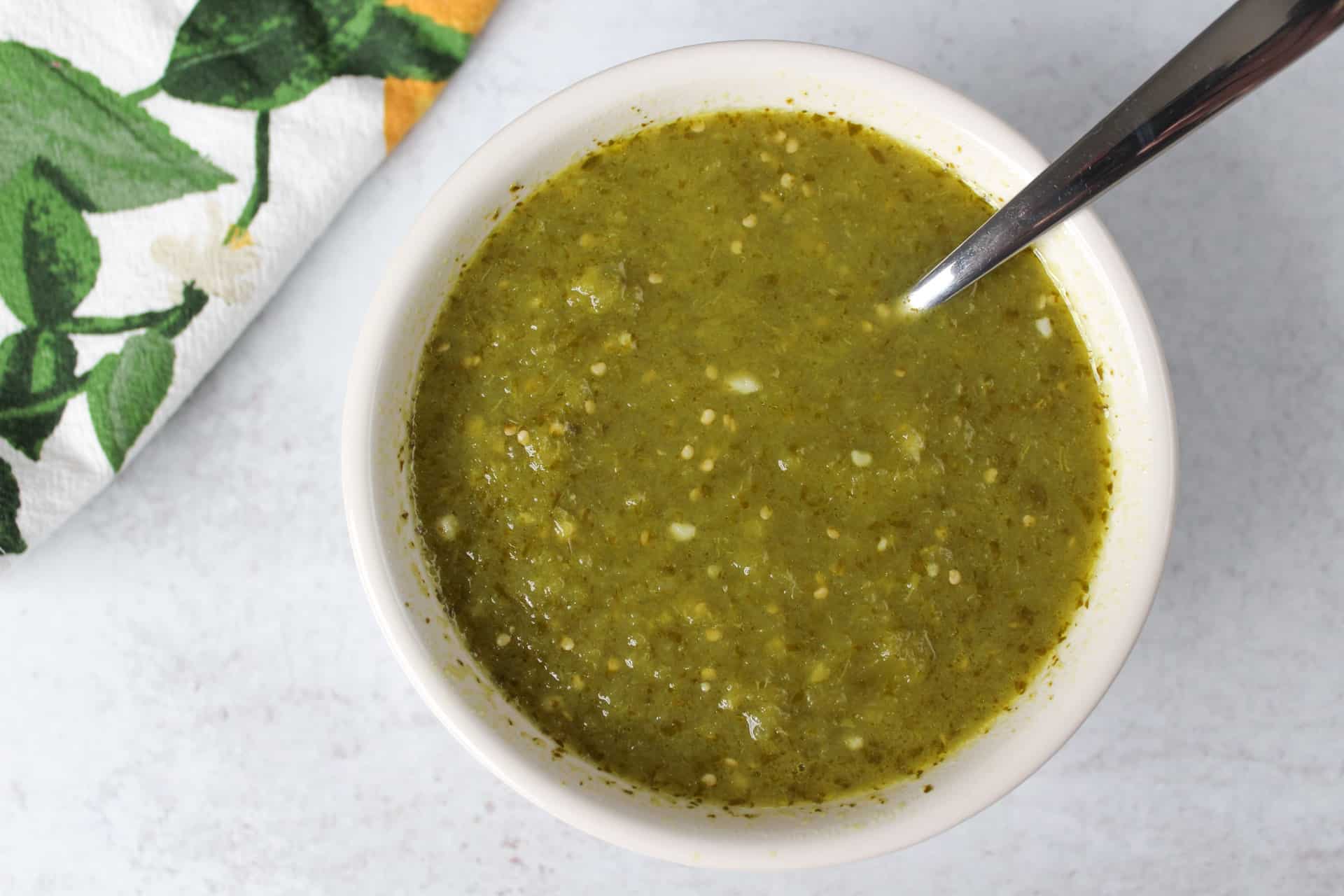 A small dish of Mexican verde sauce with a spoon.