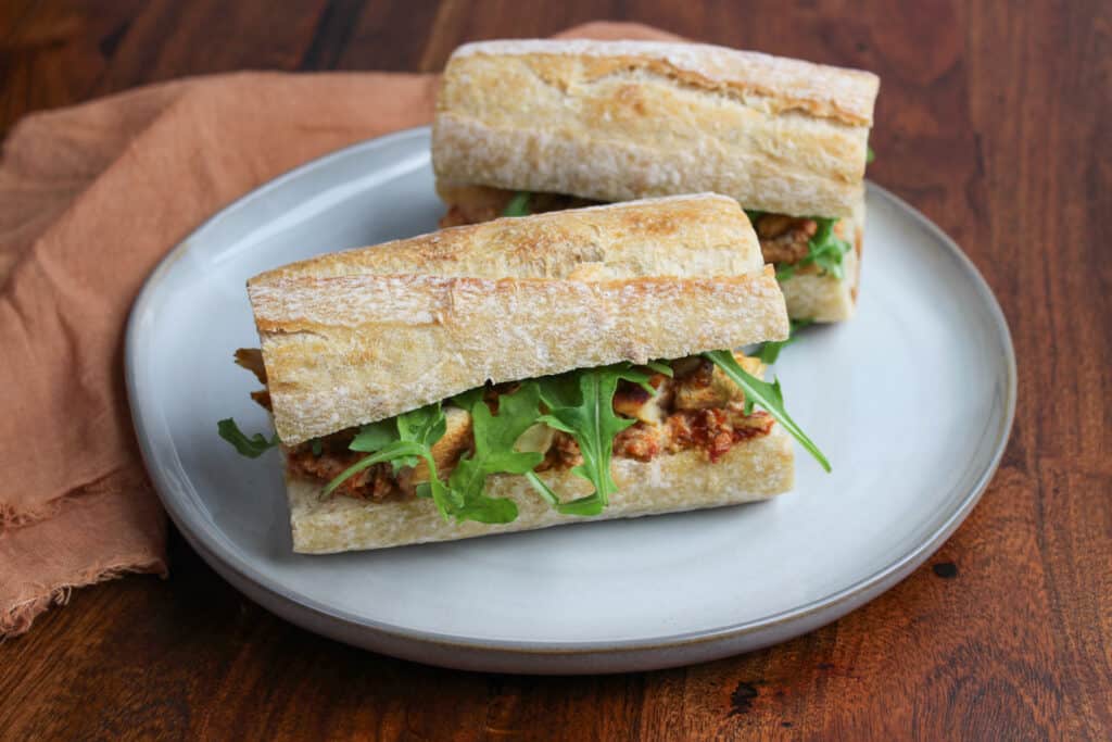 A chicken and goat cheese sandwich made with sun dried tomatoes, arugula, and caramelized onions.