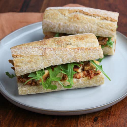 A chicken and goat cheese sandwich made with sun dried tomatoes, arugula, and caramelized onions.