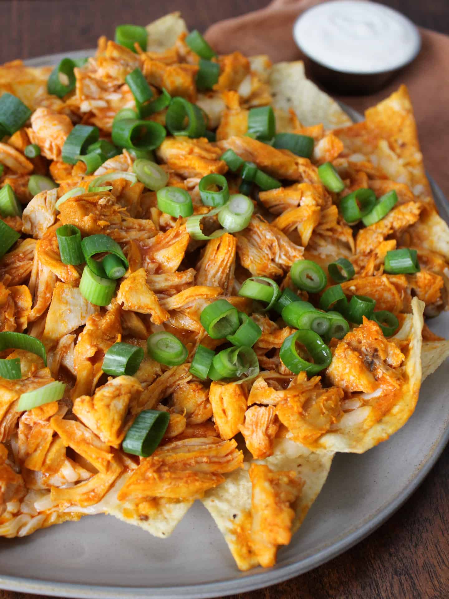 A plate of loaded buffalo chicken nachos topped with scallions.