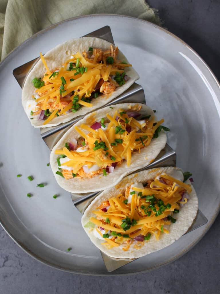 A plate of shredded buffalo chicken tacos topped with cheddar cheese.