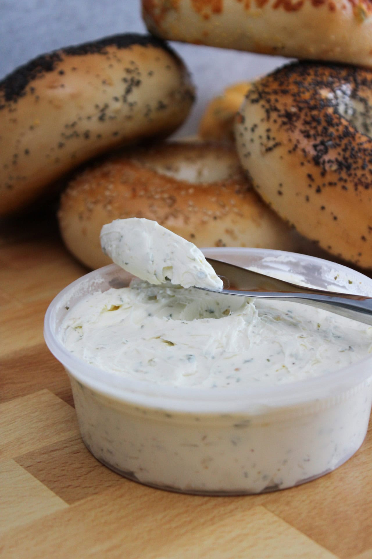 A homemade flavored garlic and herb cream cheese in a tub with a pile of various bagels.