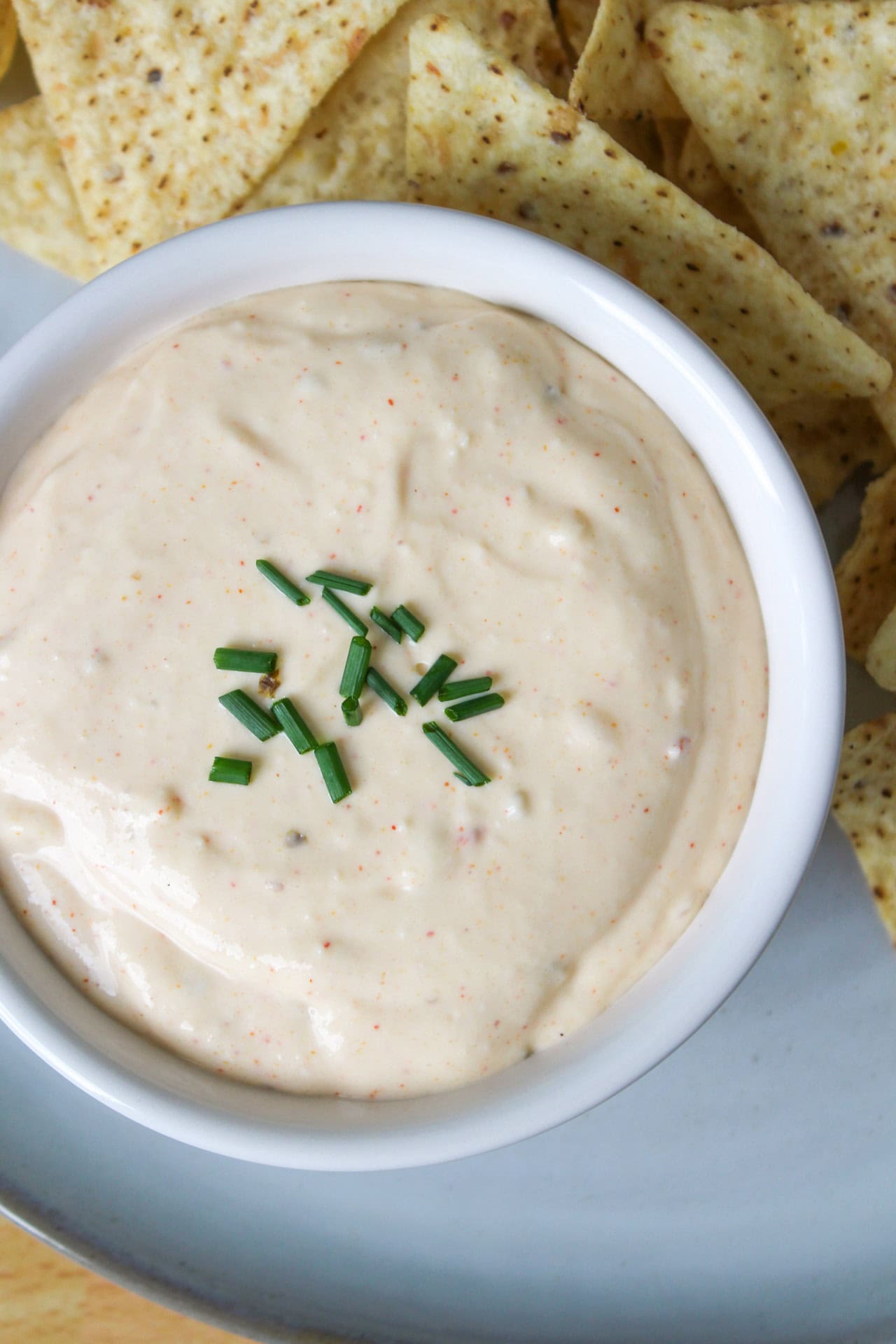 A white bowl filled with a creamy cottage cheese queso topped with chopped chives.