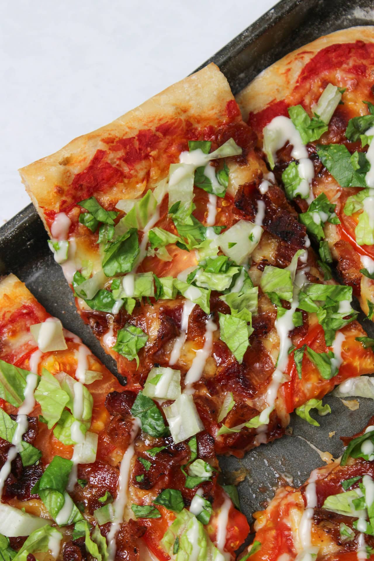 A slice of BLT pizza drizzled with garlic aioli in a sheet pan.