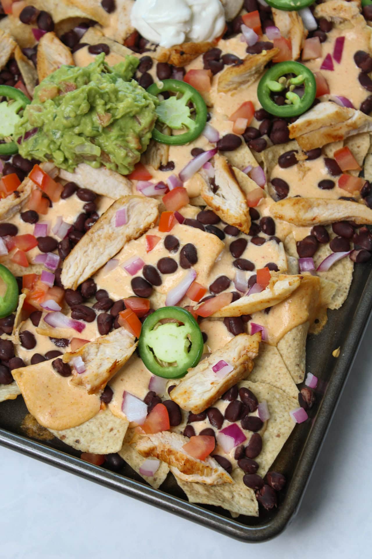 High protein nachos with cottage cheese nacho sauce, black beans, Greek yogurt, guacamole, grilled chicken, and fresh produce. 