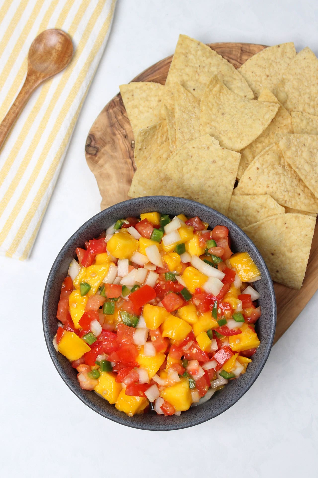 Pico de gallo with mango in a stone bowl served with a side of tortilla chips on a wooden serving tray.