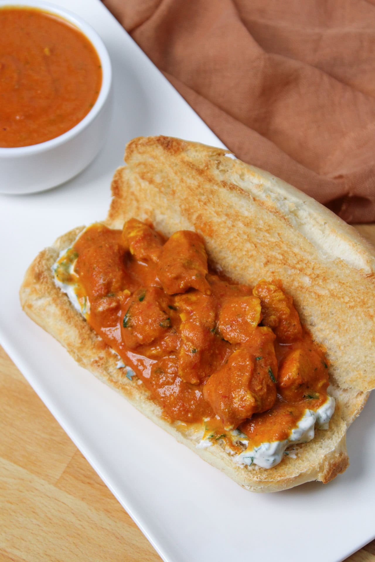 An Indian butter chicken sandwich with a creamy raita sauce on a sub roll and more sauce for dipping.