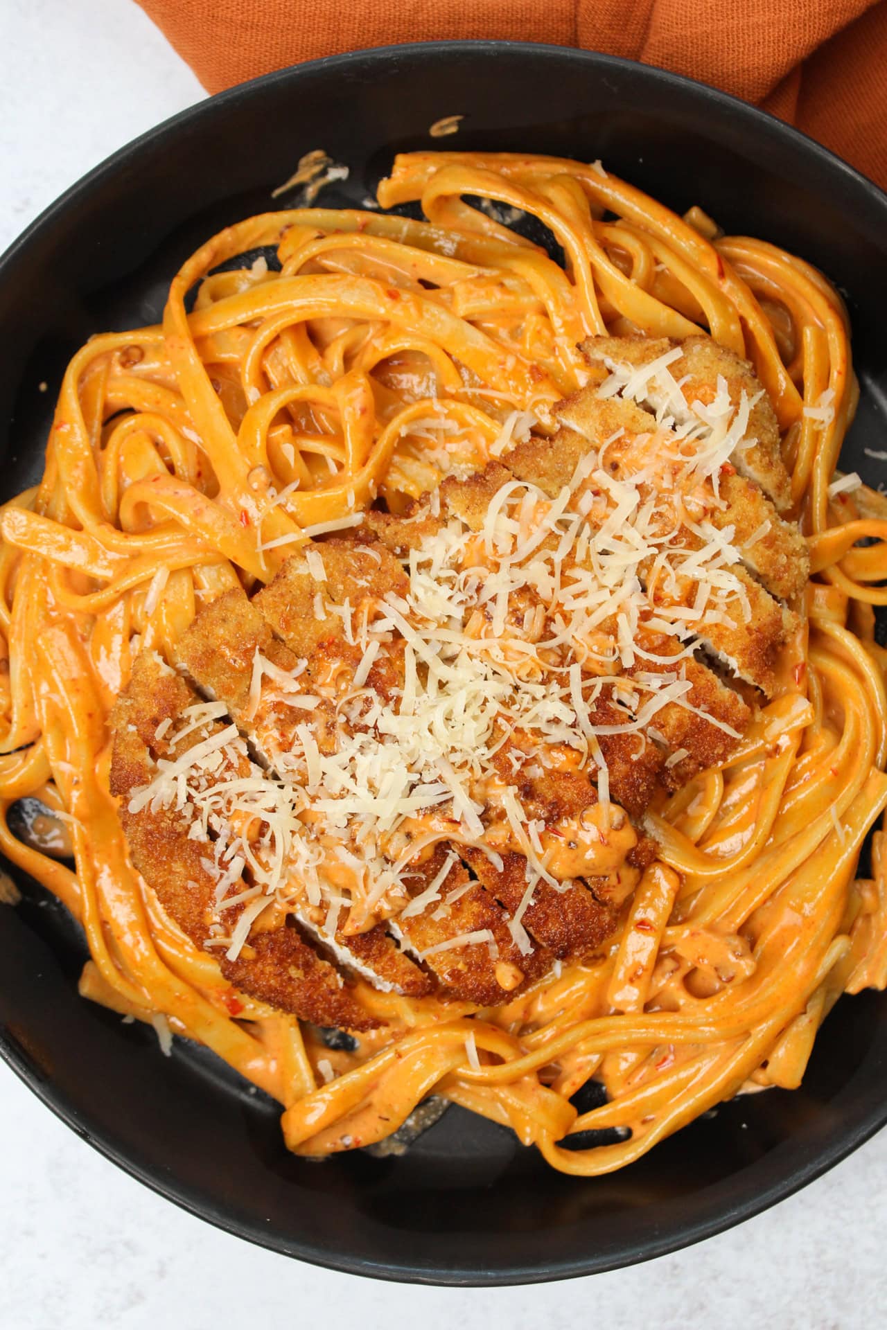 Crispy fried chicken on a creamy chipotle pasta topped with shredded parmesan in a black bowl.