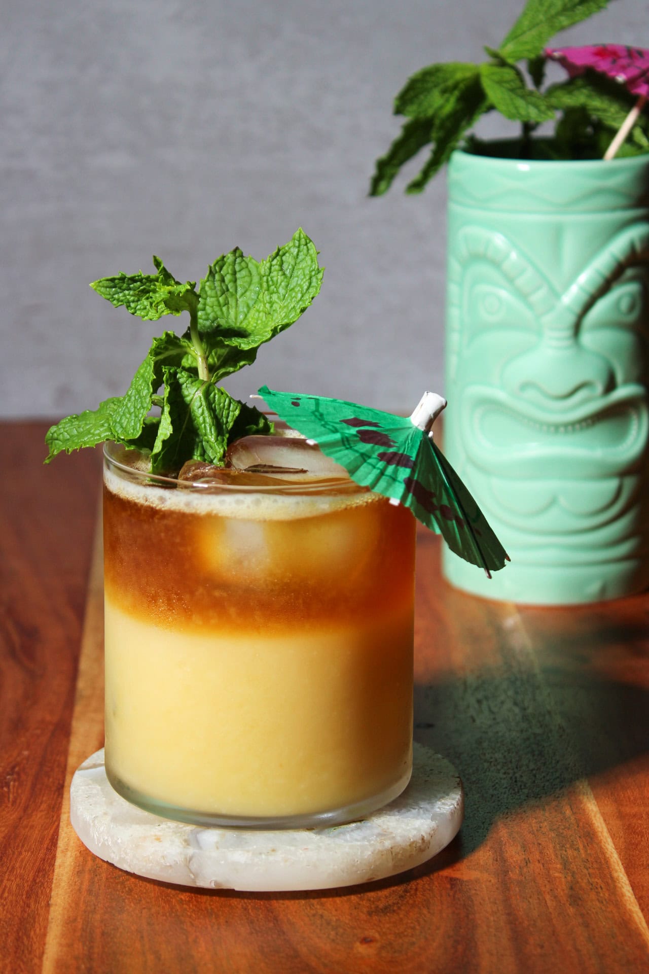 Mango mai tai tiki cocktail with a dark rum float, mint sprig, and cocktail umbrella.