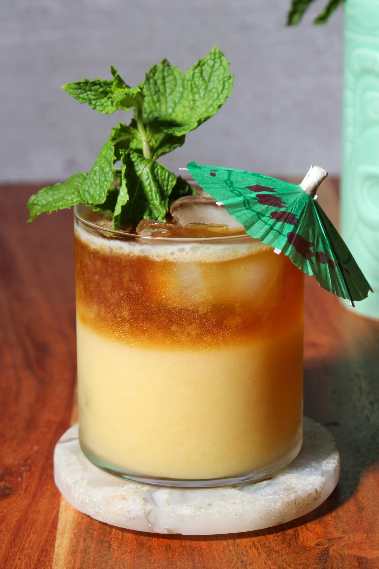Mango mai tai with dark rum float garnished with a mint sprig and a cocktail umbrella.