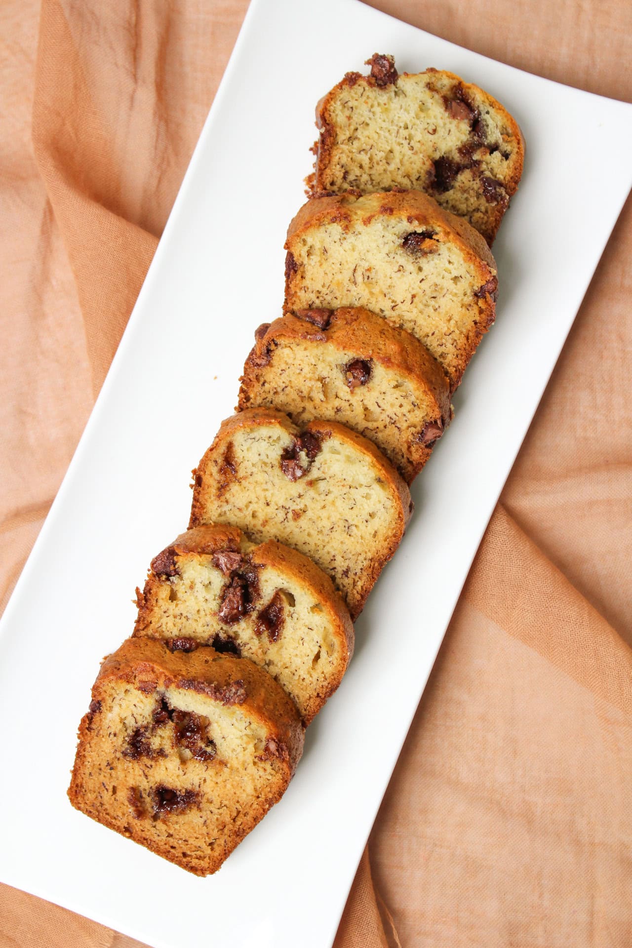 Slices of freshly baked moist chocolate chip banana bread on a white ceramic serving platter.