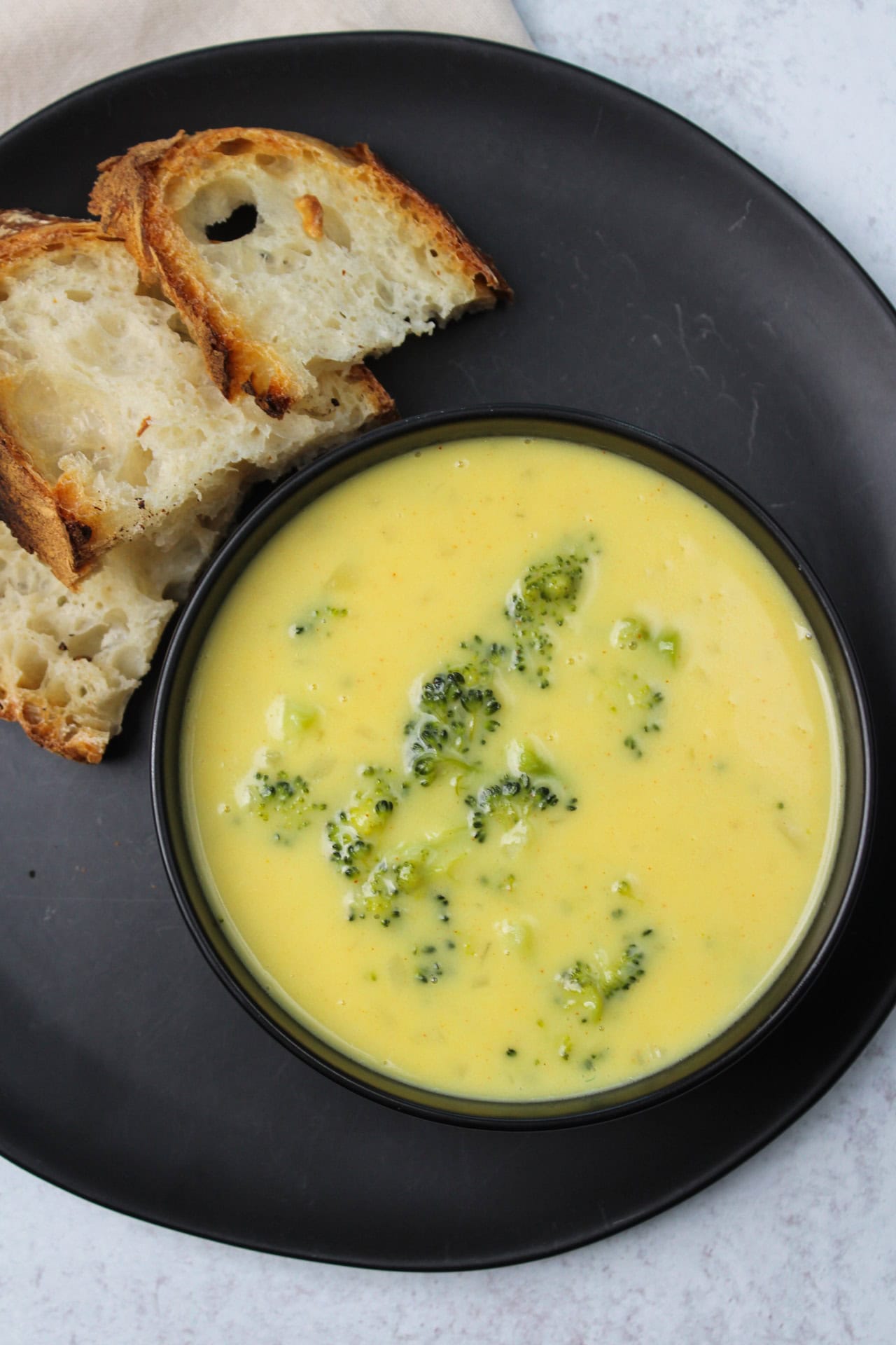 A bowl of creamy broccoli cheddar soup served with a side of fresh baked bread.