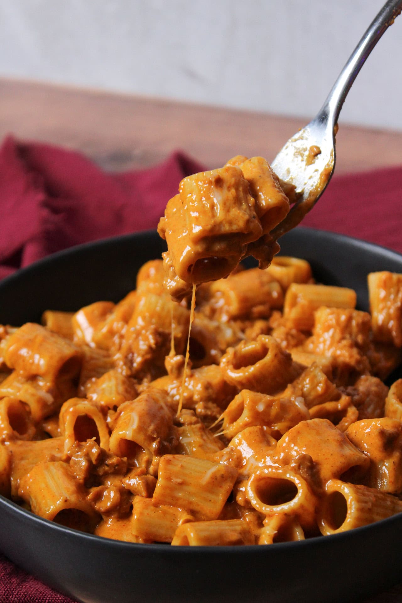 Cheezy Mexican chorizo pasta made with rigatoni being picked up out of a shallow bowl with a fork.