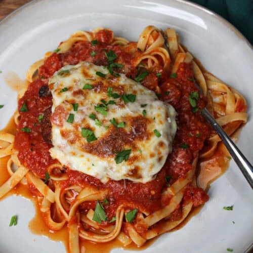 Chicken parm on a plate of pasta.