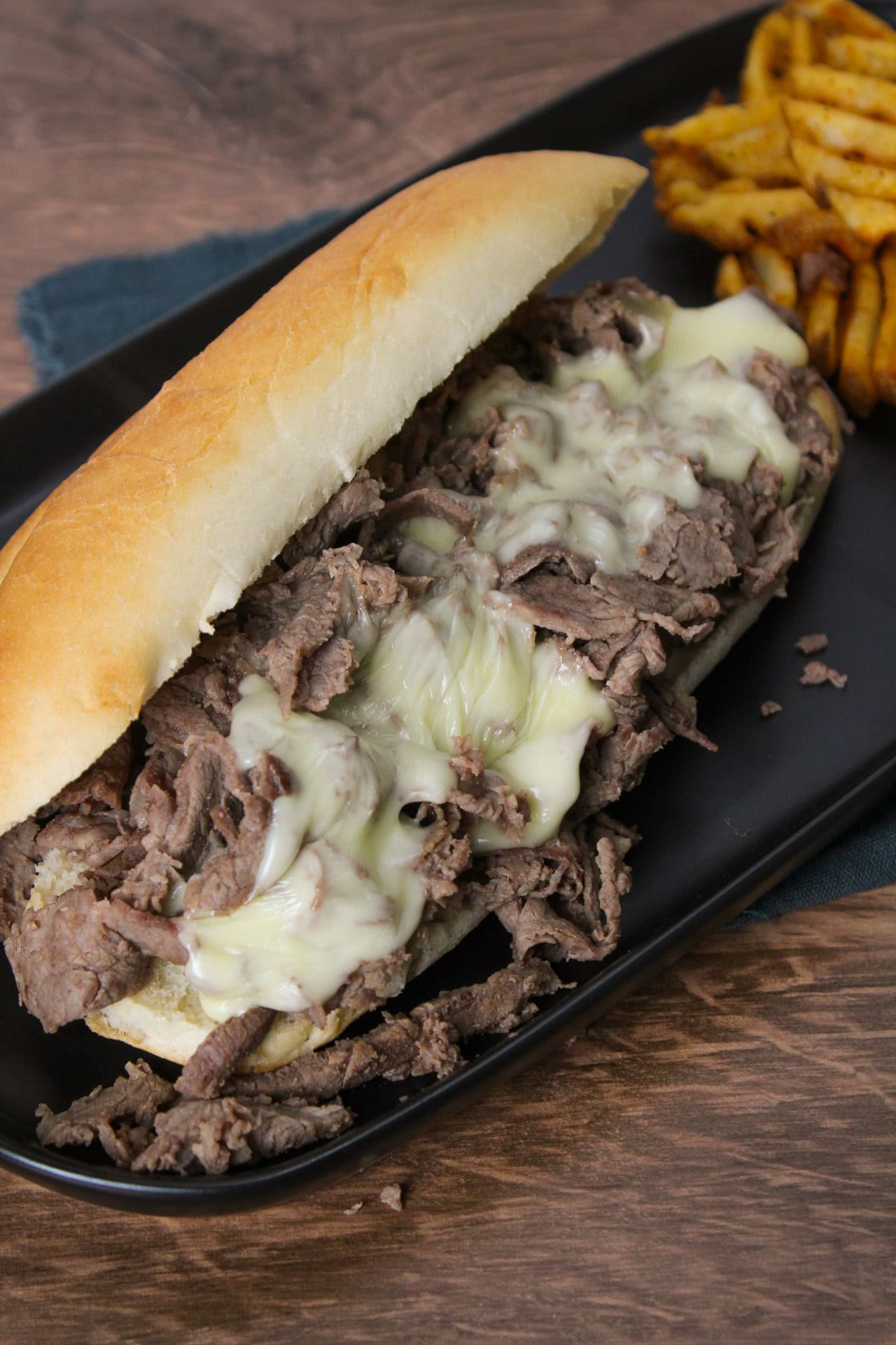 A Philly cheesesteak hoagie on a long black plate.