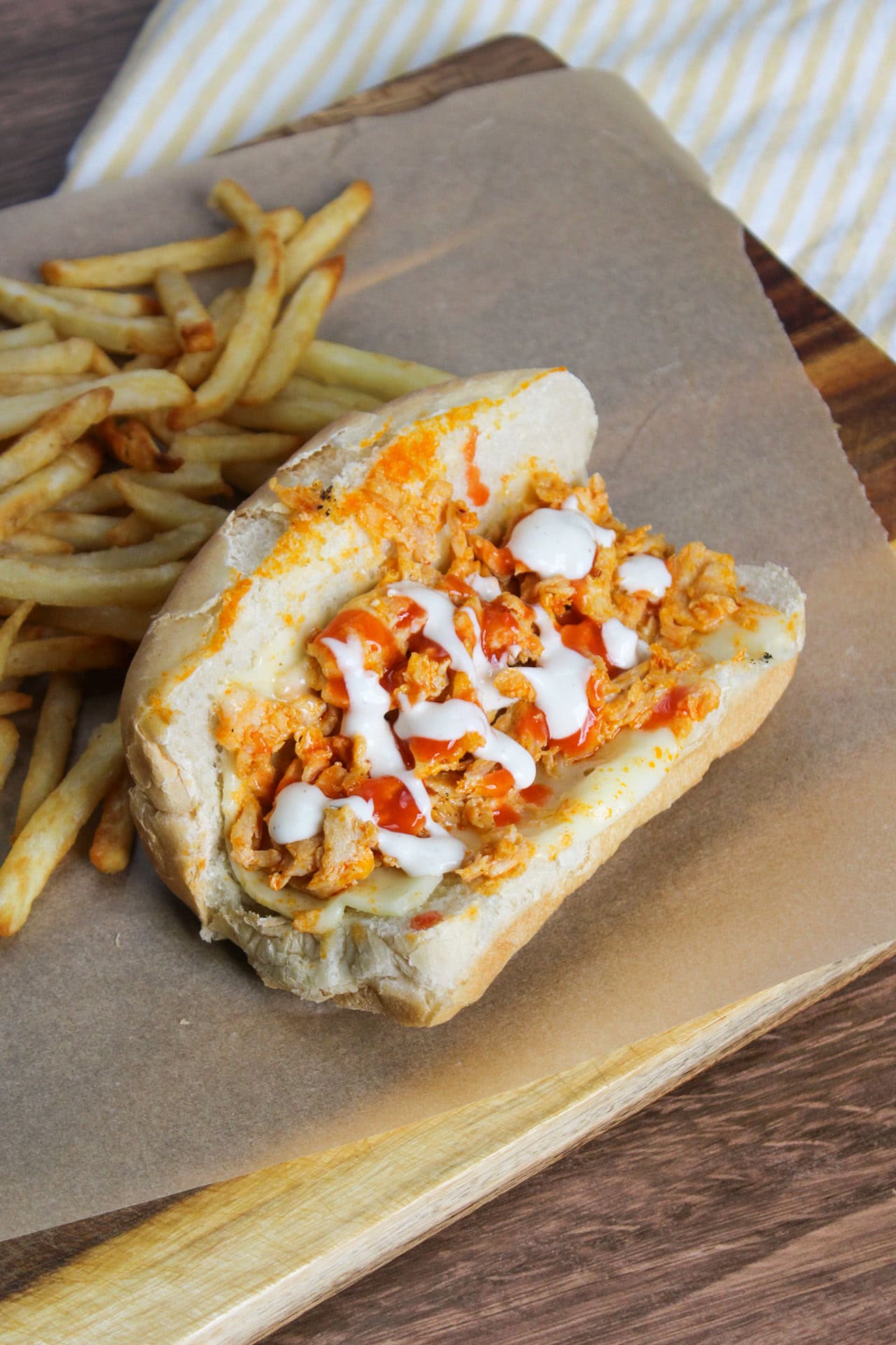 A saucy, cheesy, buffalo chicken cheesesteak on a sub roll topped with hot sauce and ranch dressing and served with fries.