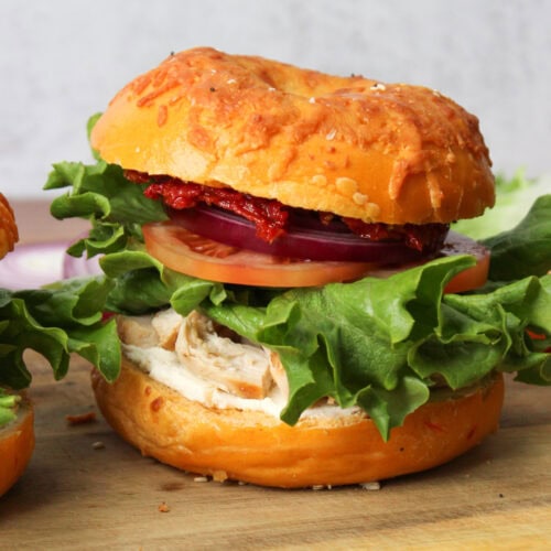 A bagel sandwich with chicken, cream cheese, and sun dried tomatoes.