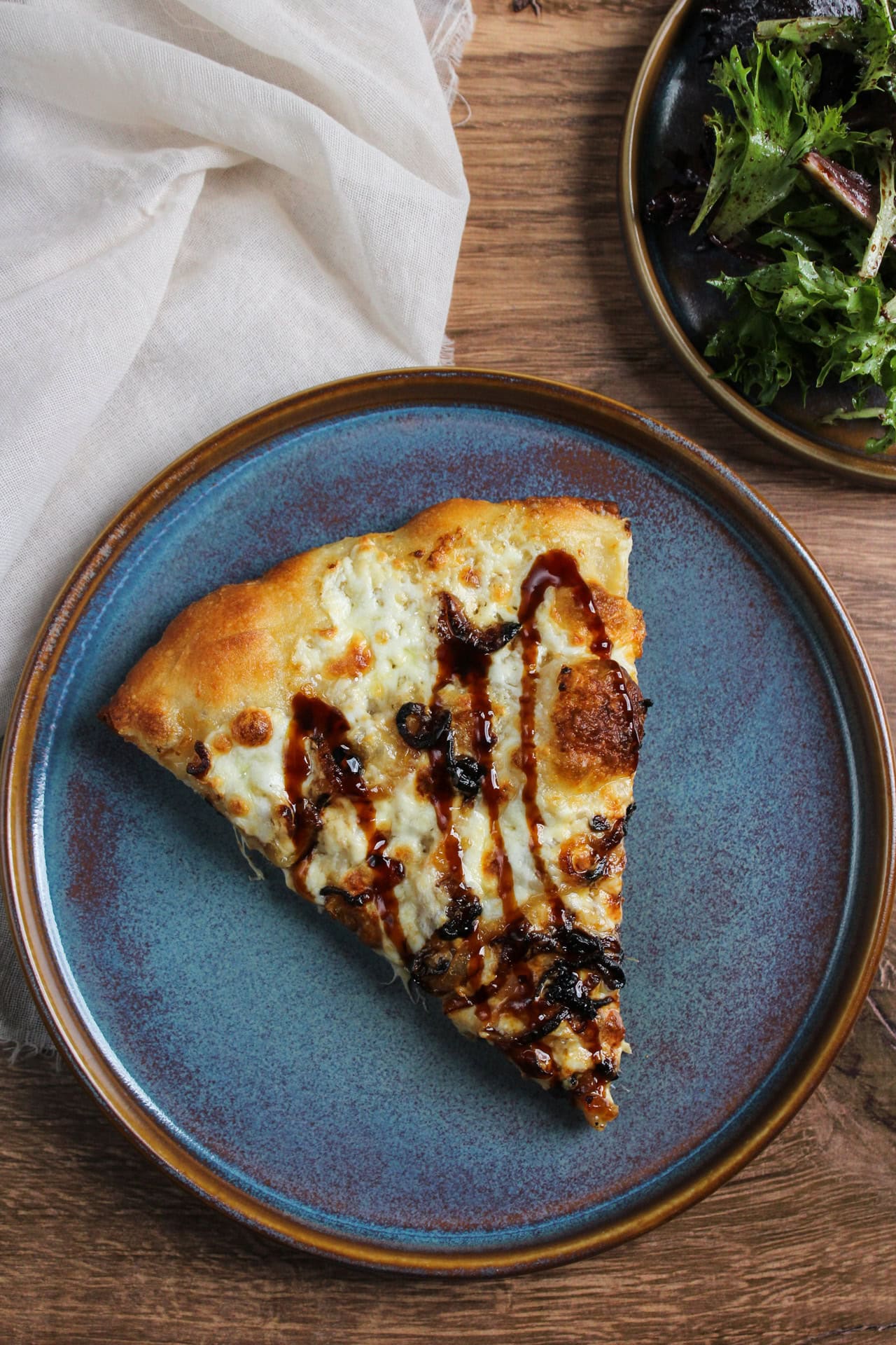 A slice of white burrata pizza drizzled with balsamic glaze on a blue stoneware plate.