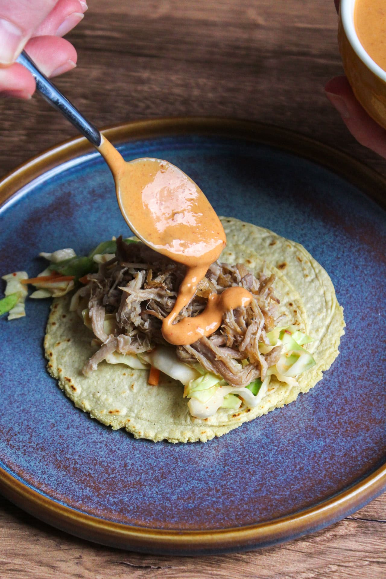 Hawaiian tropical BBQ aioli being drizzled onto a pulled pork taco on a corn tortilla.