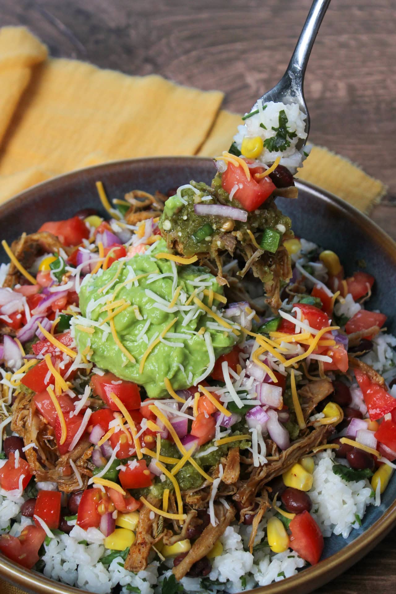 A carnitas bowl with verde sauce, pico de gallo, mexican cheese, beans, corn, and guacamole.